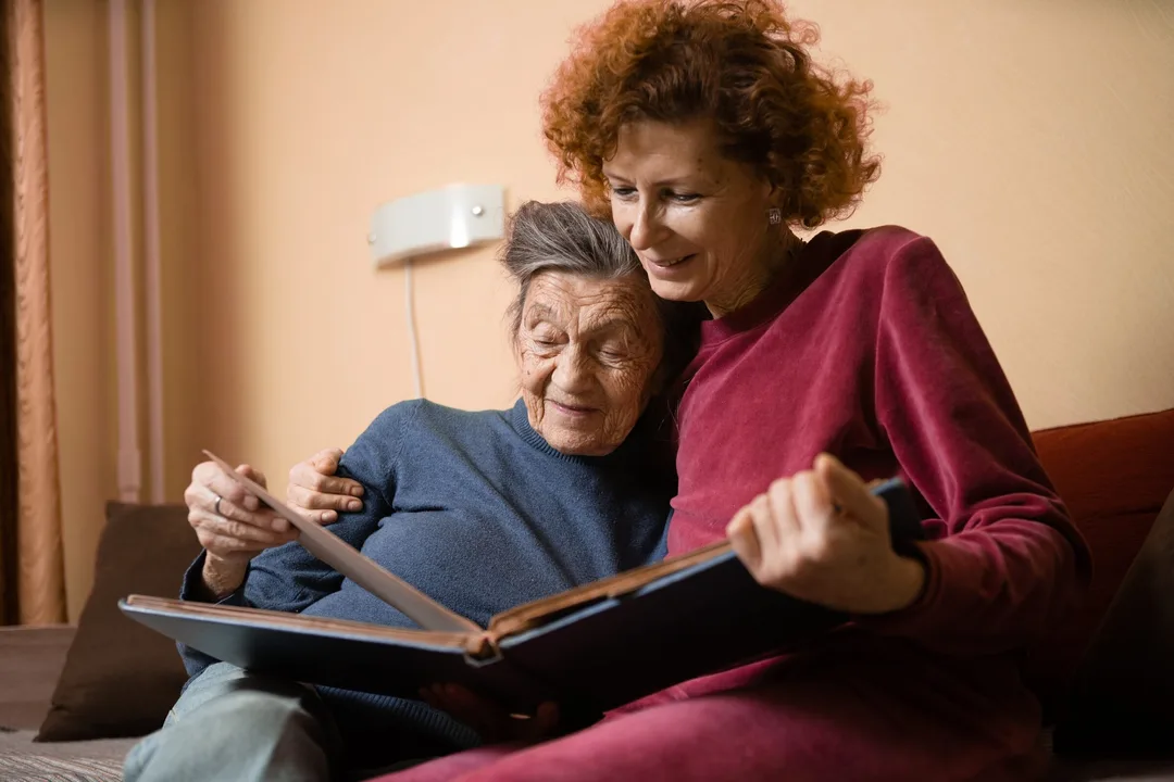 A caregiver and older woman looking through a family photo album together